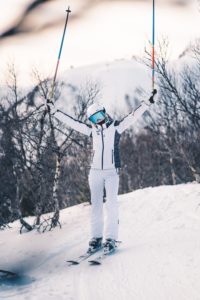 Female skier on the summit of Whiteface Mountain holding her poles up ion the air